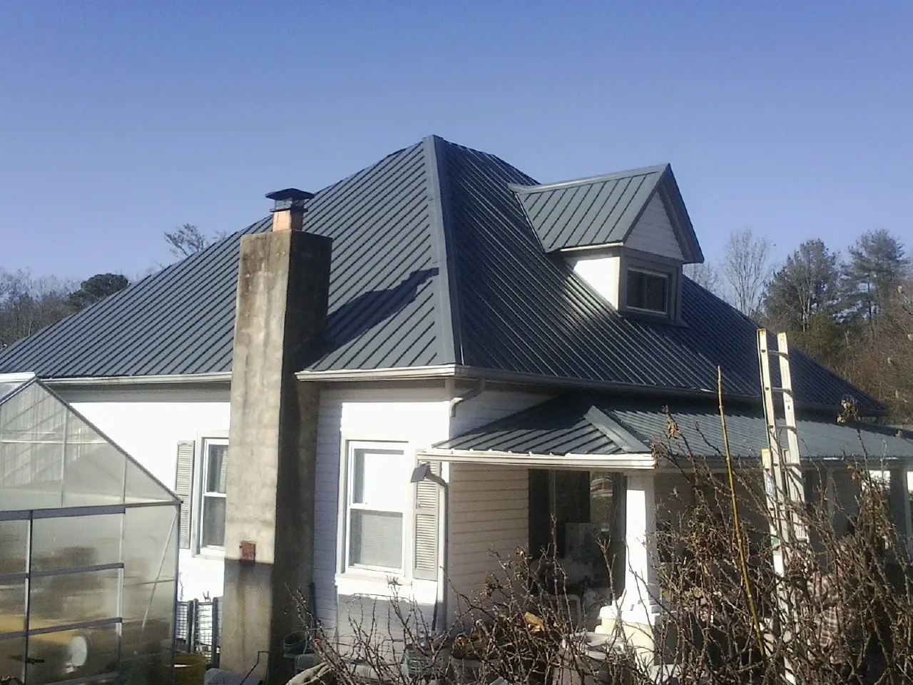 Dark blue standing seam metal roof on a white farmhouse with dormer — Slate & Tile Roof Repair by Roofing Brothers in Milo