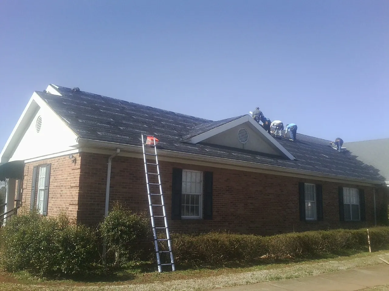 Crew tearing shingles off a brick ranch roof with a ladder set — Emergency Roof Repair work by our crew in Milo
