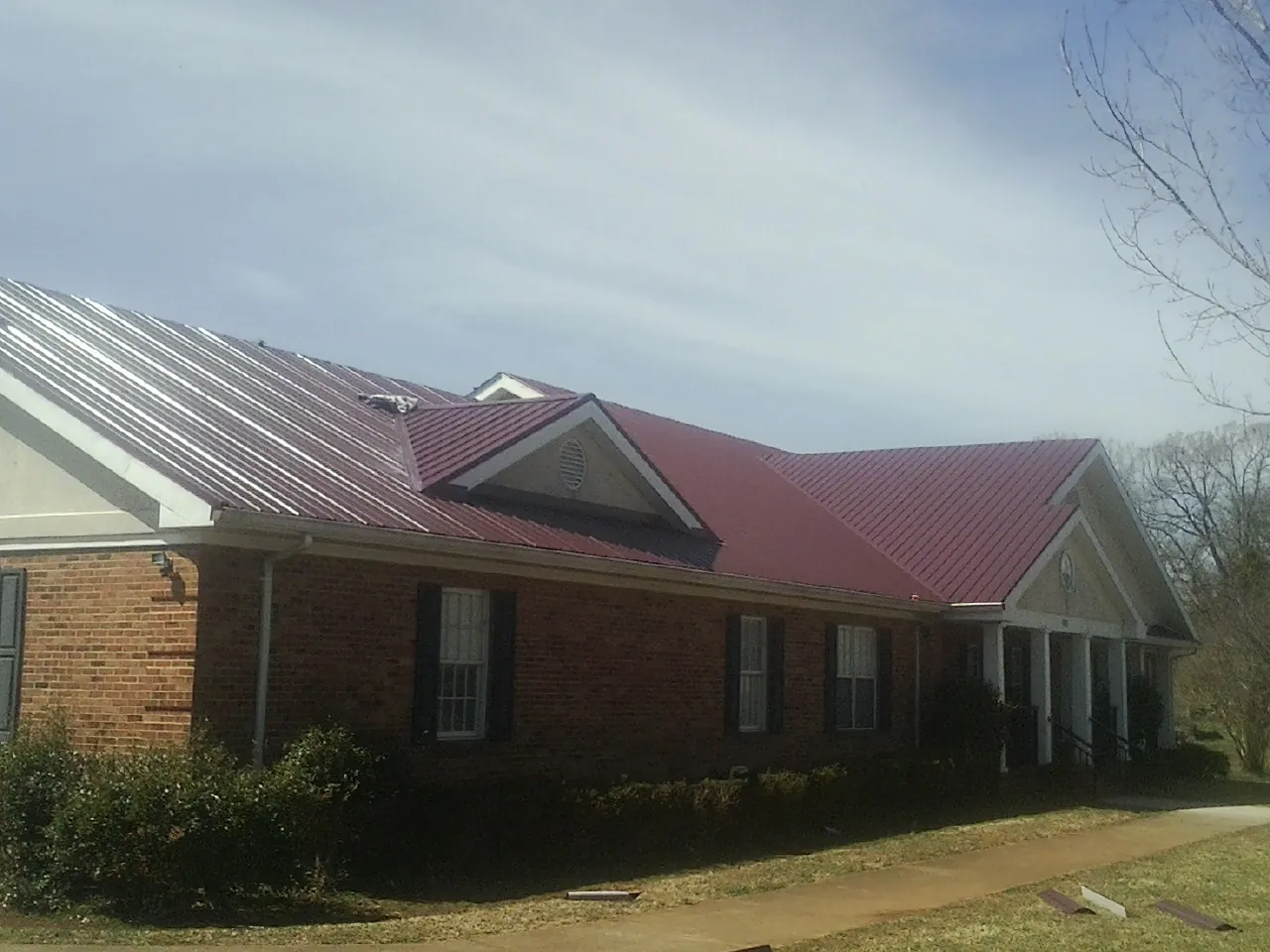 Red metal roof with gabled entries on a long brick building, from a Hail Damage Roof Repair job in Milo