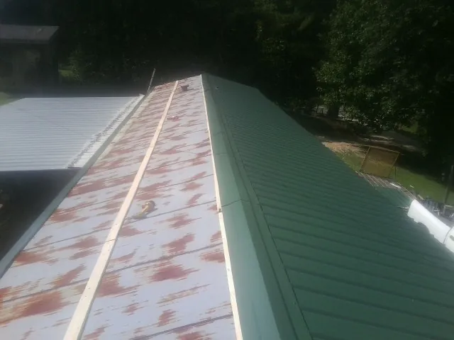 Old rusted panels beside newly installed green metal roofing — Wind Damage Roof Repair by Roofing Brothers in Milo