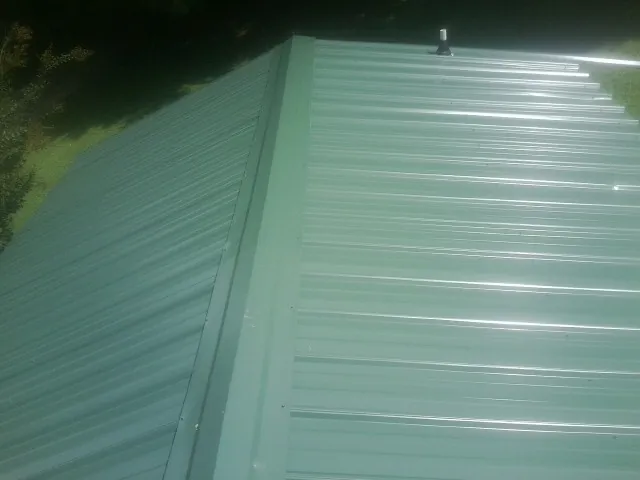 New green metal panels meeting at the ridge of a roof — Flat Roof Repair work by our crew in Milo
