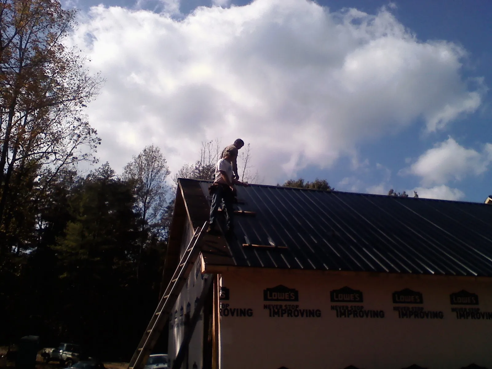 Roofer fastening dark metal panels high against a cloudy sky, from a Roof Inspection job in Milo