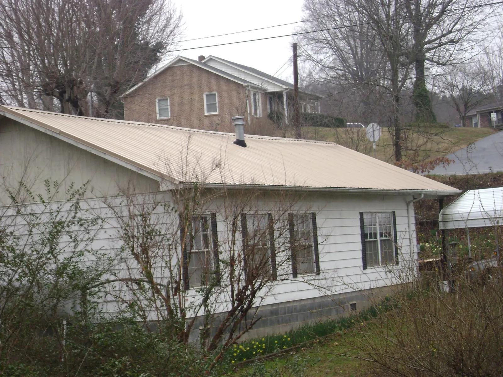 Tan metal roof on a white sided house set into a hillside — Commercial Roofing by Roofing Brothers in Milo